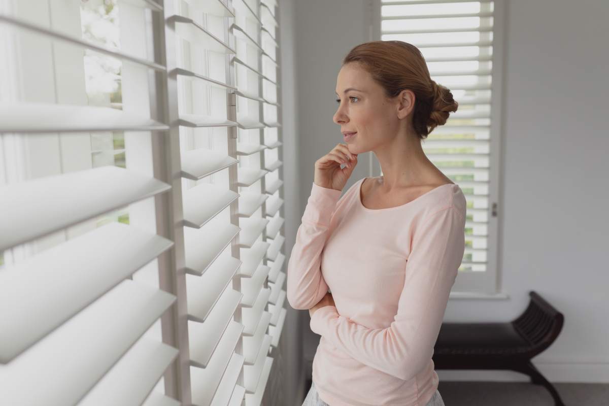 Side view of beautiful thoughtful Caucasian woman looking outside through window in a comfortable home