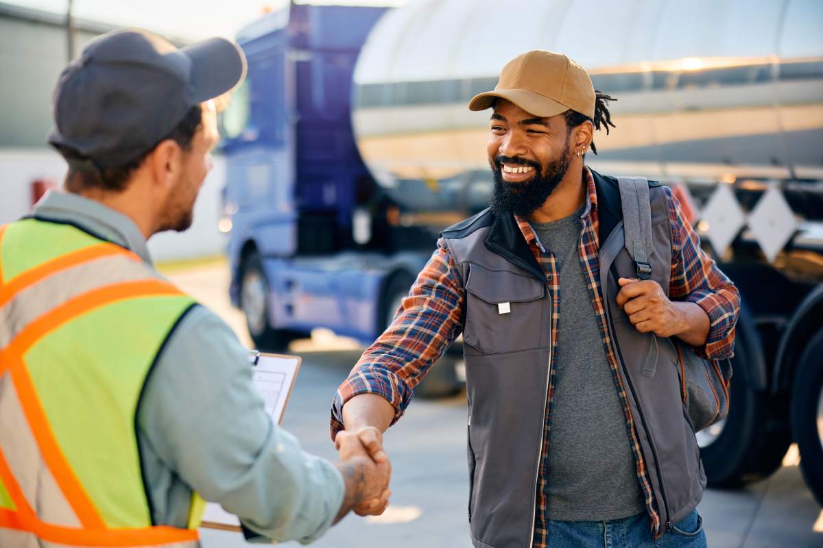 Happy African American driver greeting a dispatcher on truck parking lot.