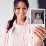 Portrait Of Female Photographer On Photo Shoot Holding Up Instant Polaroid Print In Studio