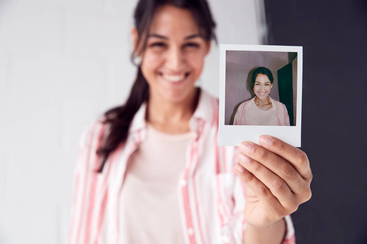 Portrait Of Female Photographer On Photo Shoot Holding Up Instant Polaroid Print In Studio