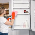 Woman in red gloves is doing cleaning and wash a refrigerator inside