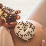 Pregnancy and nutrition. Pregnant woman enjoying donuts and tea in bed, free space. Concept of expectation and health