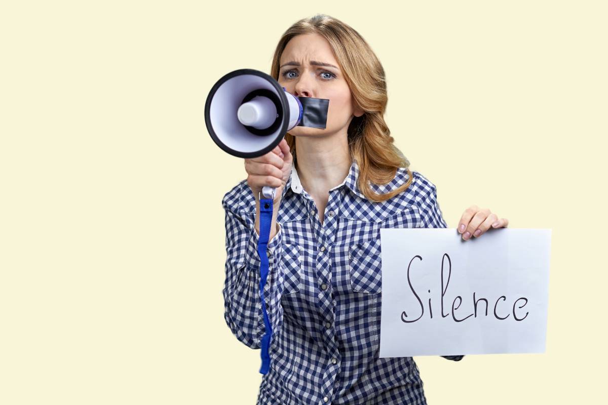 Young blonde woman struggles to speak in megaphone because of mouth taped.